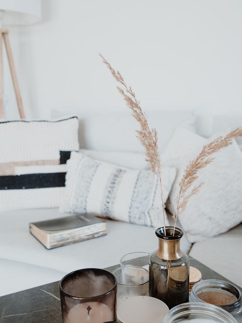 Closeup einer Sofaecke mit einem weißen Sofa vor dem ein dunkler Tisch mit Pampasgras steht.