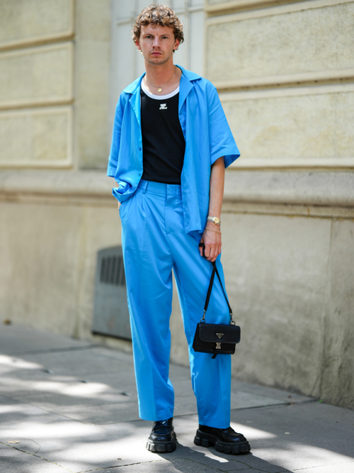 Street Style Look von der Paris Fashion Week, wo ein Gast ein blaues Kurzarmhemd mit gleicher Hose, einem schwarzen Tanktop und Handtasche trägt.