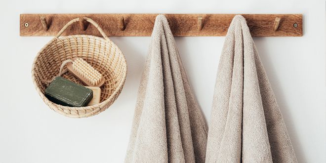 Holzleiste an einer Wand mit Haken und Handtüchern, Seife und Korb daran hängend.