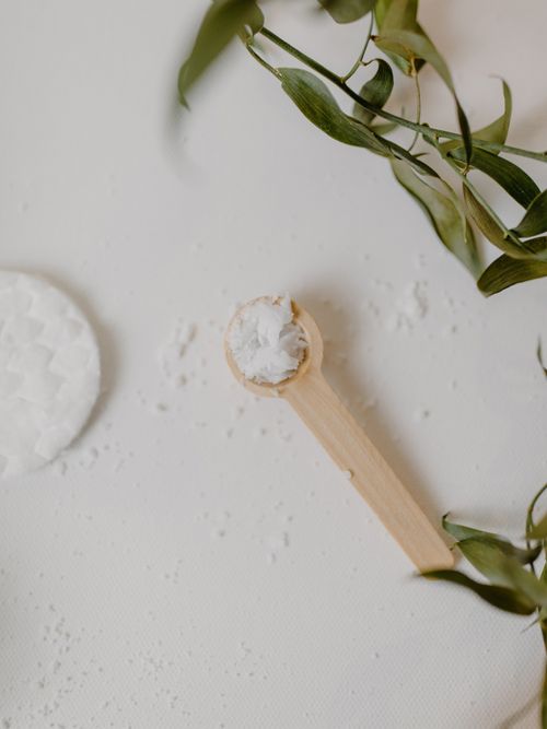 Ein Holzlöffel mit weißer Masse und ein Blätterzweig auf einem weißen Hintergrund.