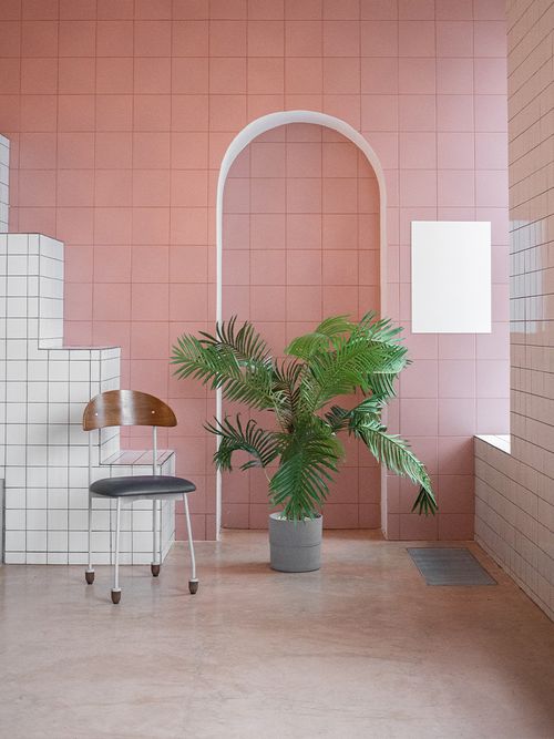 Ein rosa und weiß gefliester Raum mit einer großen Palme und einem schwarzen Stuhl.