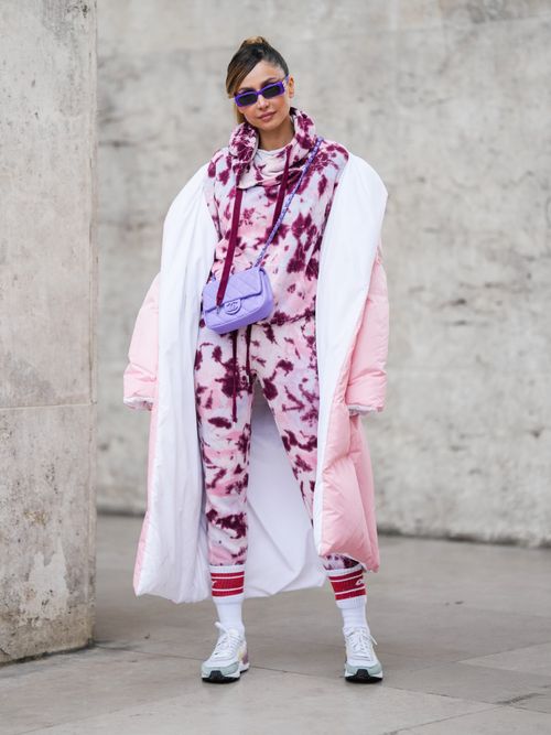 Patricia Gloria Contreras trägt einen Jogginganzug in Batikmuster mit blauer Sonnenbrille und fliederfarbener Tasche, mit Roten Socken und Sneakers in Paris