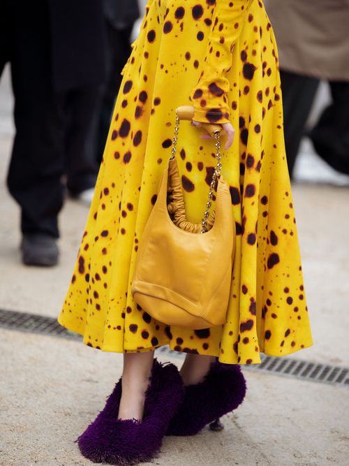 A guest wears yellow dress with dark brown spots and fluffy purple shoes outside Loewe during the Womenswear Fall/Winter 2024/2025 as part of Paris Fashion Week on March 01, 2024 in Paris, France.