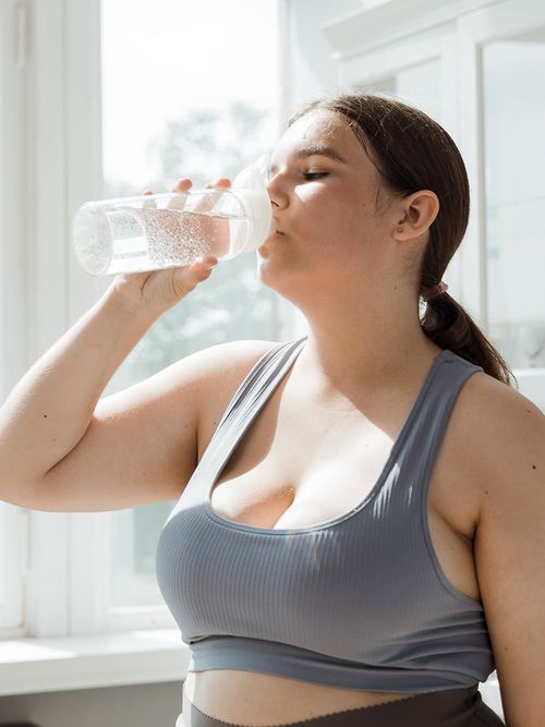 Frau in grauem Sport-BH die gerade Wasser trinkt.