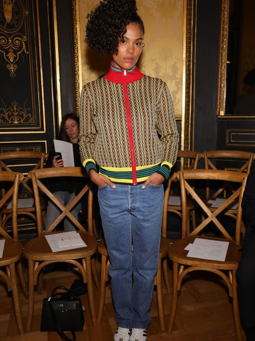 Tina Kunakey wears a striped zip-up jumper, straight blue jeans, and white tennis shoes.