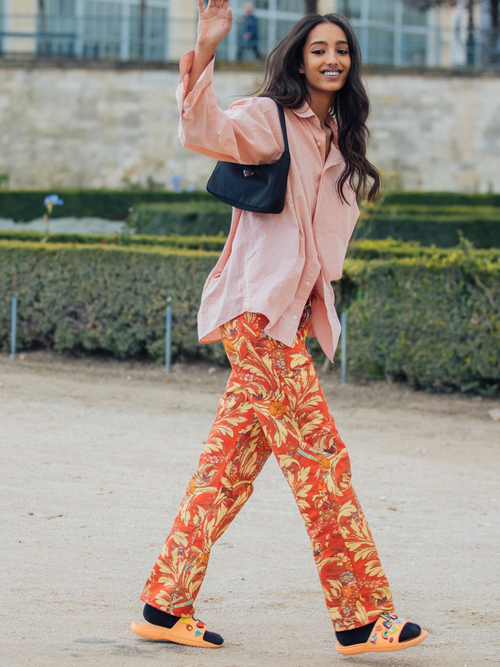 Model Mona Tougaard trägt eine lachsfarbene Bluse, eine orangefarbene bunte Hose mit schwarzen Socken und Pantoffeln. Dazu eine Prada Tasche auf der Paris Fashion Week.