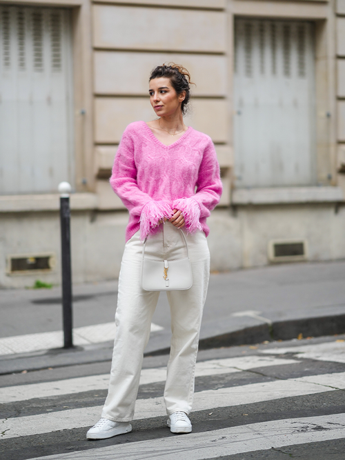 Weiße Sneakers und Hose werden zu einem pinken Strickpullover kombiniert.