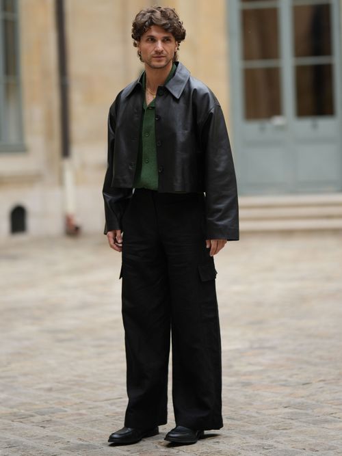 Street Style Look von Paris, wo ein Mann eine Lederjacke mit grünem Hemd und schwarzer weiter Hose trägt.