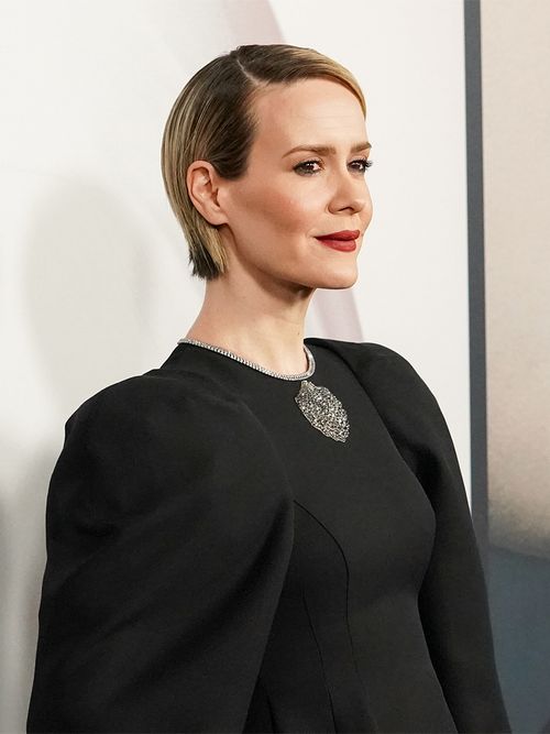 Schauspielerin Sara Paulson in einem schwarzen Kleid mit einer aufgenähten Brosche.
