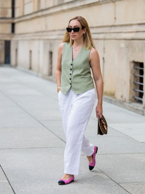 Sonia Lyson trägt eine hellgrüne Anzugweste, weiße Leinenhose, schwarze Sonnenbrille und Ballerinas in Berlin.