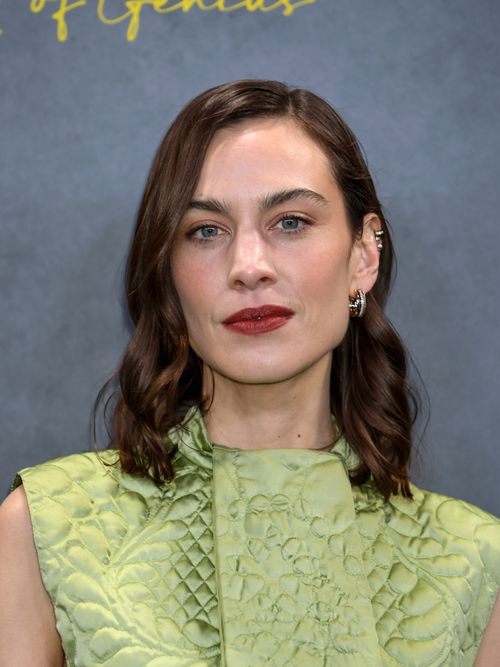 Alexa Chung trägt ein grüßes Kleid mit Schluppe und hat gewelltes Haar zu einem Seitenscheitel auf einer Fashion Show in London.
