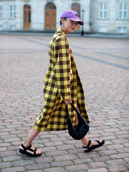 Streetstyle mit einem gelb karierten Mantel, einer lila Cap und schwarzen Teva Sandalen.