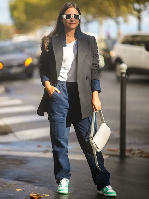 PARIS, FRANCE - OCTOBER 05: A guest wears white sunglasses, a white ribbed t-shirt, gold necklace, a black long blazer jacket, navy blue cargo pants, white latte leather crocodile pattern handbag, white and green leather Air Force One sneakers from Nike, outside Lacoste, during Paris Fashion Week - Womenswear Spring Summer 2022, on October 05, 2021 in Paris, France. (Photo by Edward Berthelot/Getty Images)