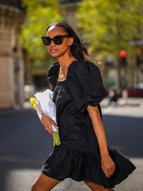 Frau mit Sonnnebrille und einem schwarzen Minikleid mit Puffärmeln.