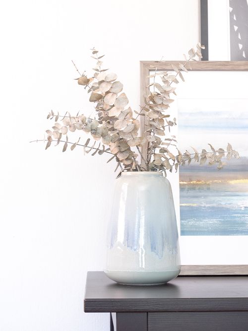 Hellblaue Vase mit getrocknetem Eucalyptus vor einem Bild.
