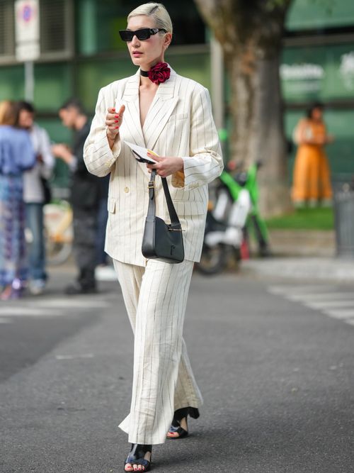 Street Style Look von der Milan Fashion Week, wo ein Gast einen Nadelstreif-Hosenanzug aus Leinen mit einem Blumen-Choker, Sonnenbrille und High Heels trägt.