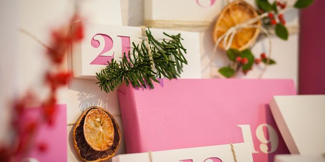 Close up von einem pink/weißen Adventskalender der mit Tannenzweigen und getrockneten Orangen geschmückt wurde.