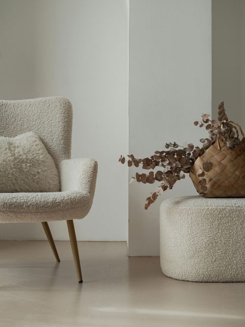 Foto von einem Stuhl, Polster und Hocker im aus Teddyfell. Dazu getrocknete Blumen in einer Vase.