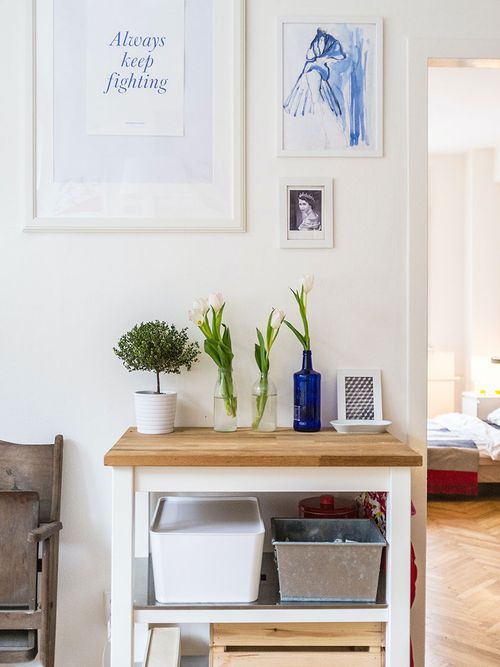 Regal vor weißer Wand mit Bildern in weißen Bilderrahmen.