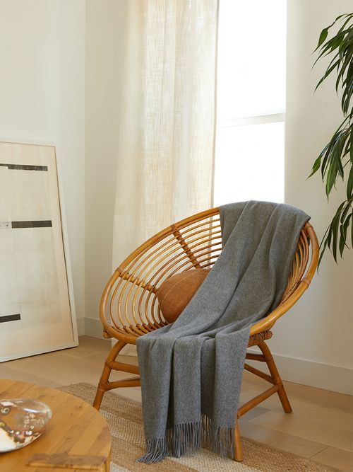 Runder Rattanstuhl über dem eine grau Decke gelegt wurde.