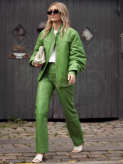Street Style Look von der Copenhagen Fashion Week, wo ein Gast ein grünes Leder-Outfit mit weißem T-Shirt und weißen Schuhen trägt.