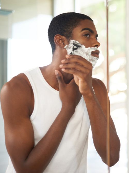 Mann, der sich vor dem Spiegel im Badezimmer rasiert.