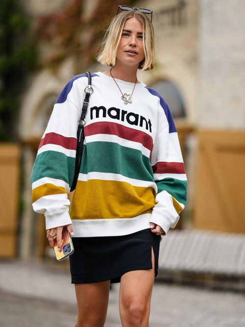 Street Style Look von der Copenhagen Fashion Week, wo ein Gast einen bunten Pullover mit schwarzem Minirock trägt.