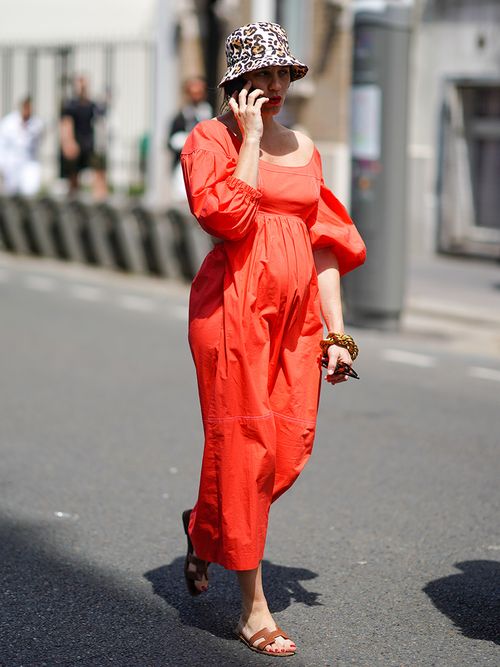 Schwangere Frau mit rotem Maxikleid und Fischerhut mit Leoprint.