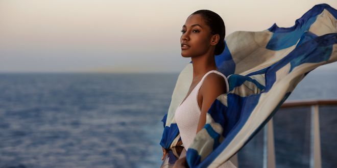 Woman wears a white bikini and a multicoloured scarf on a cruise ship balcony.