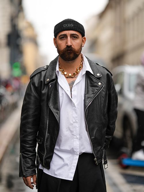 Street Style Look von der Milan Fashion Week, wo ein Gast eine Lederjacke, weißes Hemd, Statementjacke, Beanie und schwarze Hose trägt.