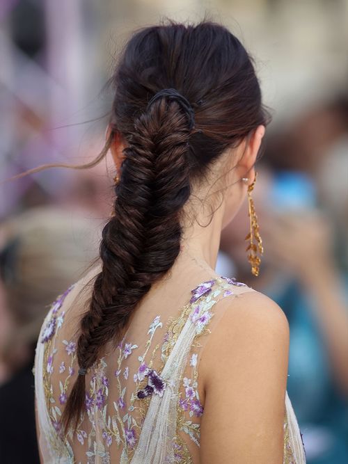 Rückansicht einer braunhaarigen Frau in einem bestickten Kleid mit einem Fischgrätenzopf.