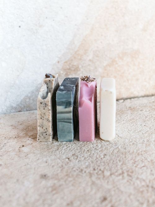 Vier handgemachte Seifen stehen vor einer beigen Steinwand.