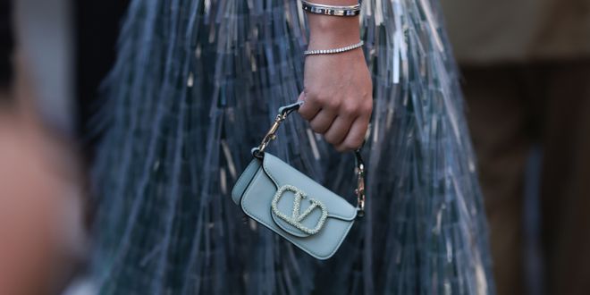 Street Style Look von der New York Fashion Week, wo ein Gast einen hellblauen Metallic-Rock, blaues Oberteil und Silberschmuck mit einer blauen Valentino Tasche trägt.