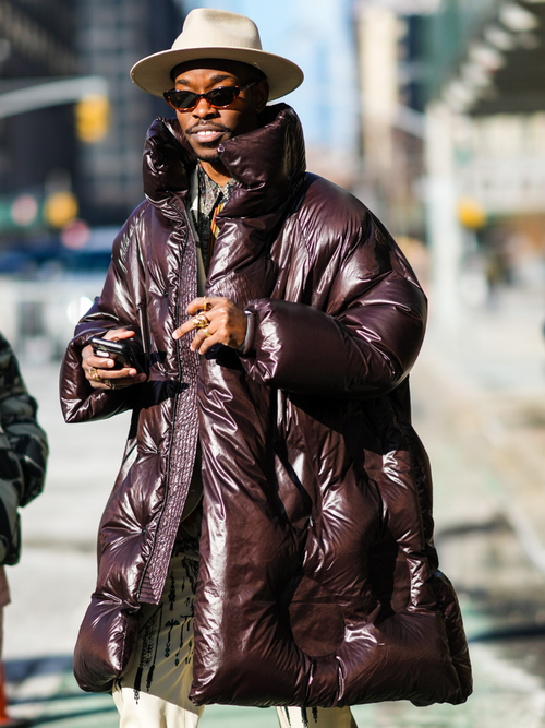 Street Style Look von der New York Fashion Week, wo ein Gast eine Metallic-Daunenjacke trägt mit Hut und Sonnenbrille