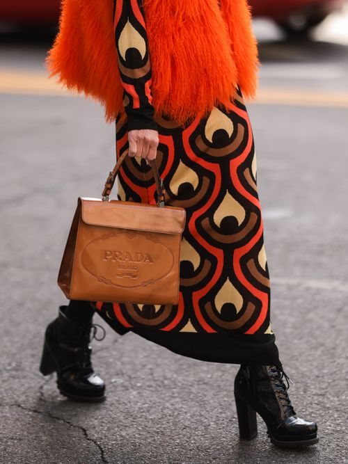 woman wearing red and black pattern dress, black heel boots and brown leather prada bag
