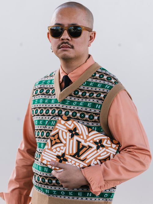 Street Style Look vom Melbourne Fashion Festival, wo ein Gast einen bunten Pullunder mit rotem Hemd, Krawatte, Sonnenbrille und Clutch trägt.