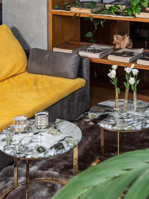 Close-up von zwei runden Marmortischen vor einem gelben Sofa.