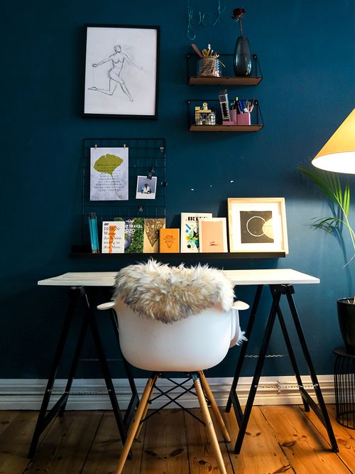 Schreibtisch mit weißer Tischplatte und Eames Stuhl vor dunkelblauer Wand mit vielen kleinen Regalen.