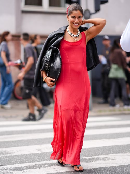 Street Style Look von der Copenhagen Fashion Week, wo ein Gast ein Maxi-Kleid in Rot mit Lederjacke und Flipflops trägt.