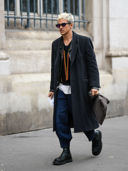 Street Style Look von der Milan Fashion Week, wo ein Gast einen schwarzen Wollmantel, blauer Hose und schwarzen Pullover mit Boots trägt.