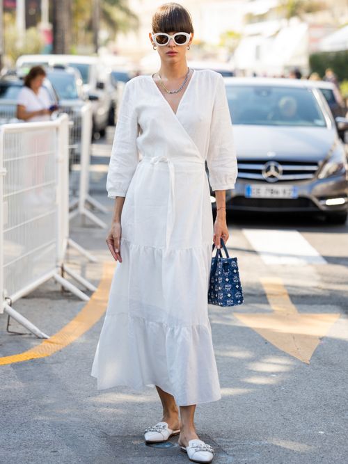 Katya Tolstova trägt ein weißes Kleid zum Wickeln, mit einer blauen Tasche und weißer Sonnenbrille in Cannes.