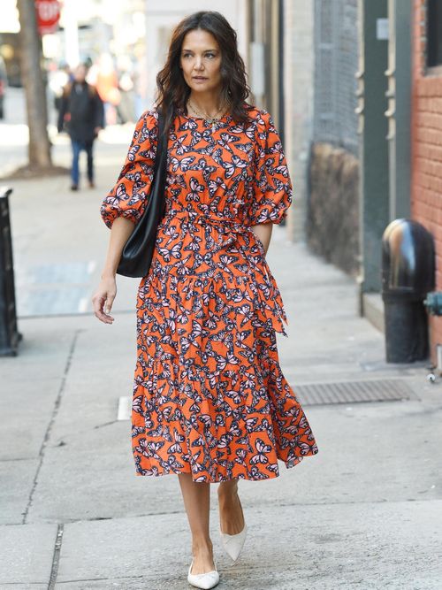 Katie Holmes in einem orangenen Kleid mit Schmetterlingen und weißen Ballerinas.