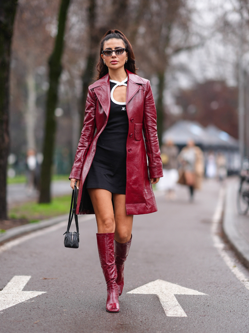 A guest wears a white and black Courreges mini dress with keyhole, a black leather bag, a red leather jacket, red leather high heels boots, sunglasses,