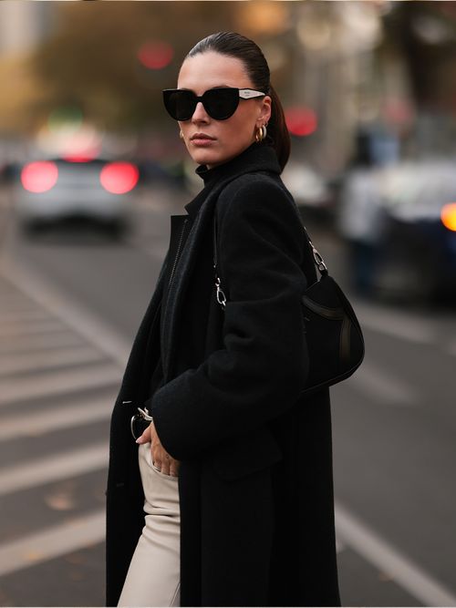 Streetstyle mit einer weißen Hose einem schwarzen Pulllover und Mantel und einer Hobo-Bag.