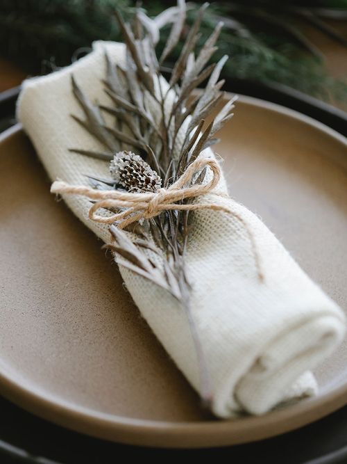 Beiges Teller mit einer weißen Stoffserviette und einem darauf gebundenen Tannenzweig.