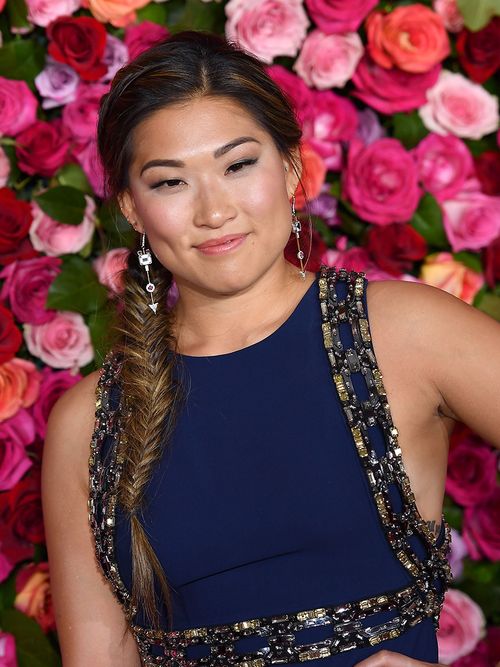 Frau mit einem Fischgrätenzopf vor einer Wand aus Blüten.