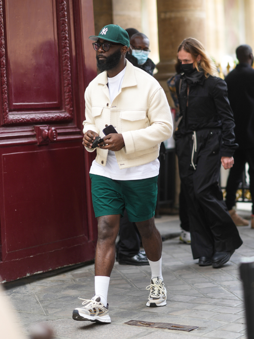 Street Style Look von der Paris Fashion Week, wo ein Gast ein weißes Overshirt mit weißem T-Shirt, grüner Hose und grüner Cap trägt.