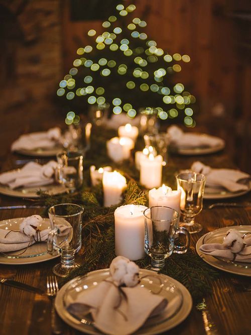 Eine Festtafel mit Tannenzweigen, beigen Tellern, Stoffservietten und Baumwollzweigen.