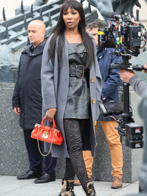 Venus William wears a black leather dress with a gray wool coat