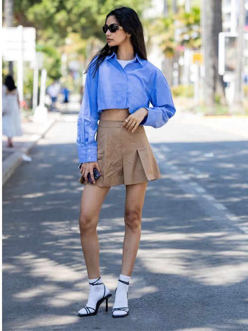 Model Sumita Bhandari trägt eine cropped Bluse mit Minirock, dazu Socken in Riemchensandaletten.